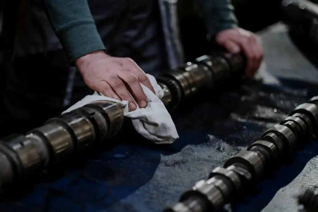 Close-up of a mechanic cleaning a camshaft with a cloth in an industrial setting.
