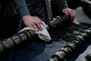 Close-up of a mechanic cleaning a camshaft with a cloth in an industrial setting.